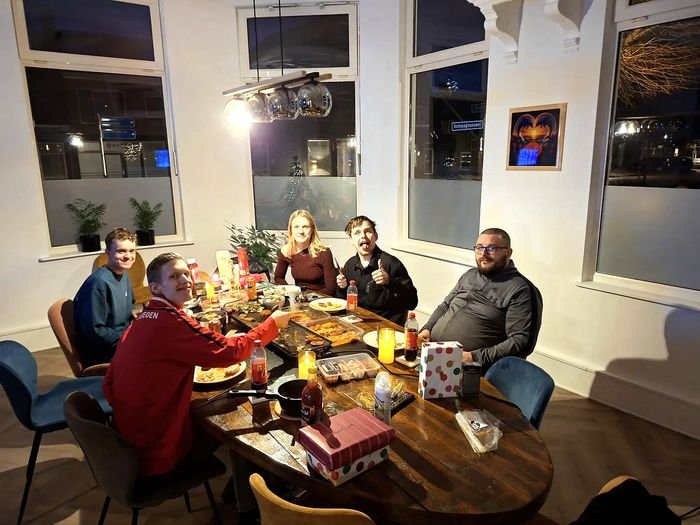 Bewoners en begeleiders eten samen aan de grote houten tafel, met kaarsen en cadeautjes op tafel.