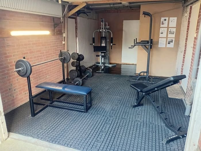 Een fitnessruimte met een halterbank, gewichten en een krachtstation.