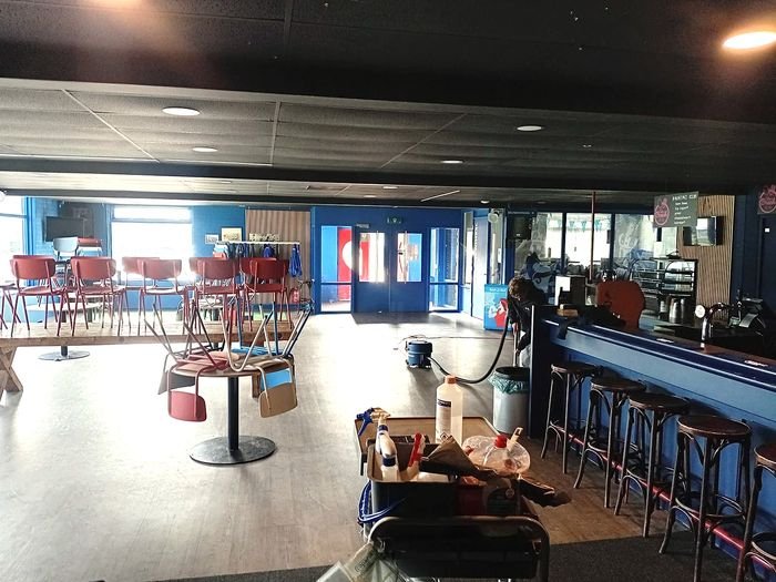 Een sportkantine met de stoelen op tafel en schoonmaakspullen bij de bar.