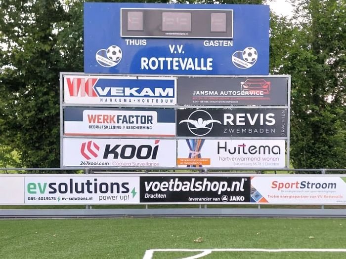 Het scorebord van VV Rottevalle boven het kunstgrasveld, met reclameborden eronder.