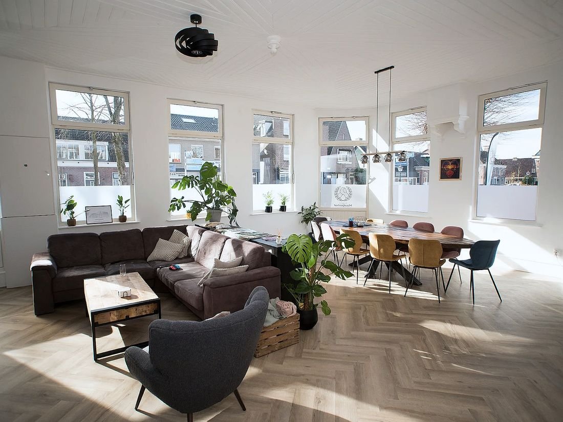 De lichte woonkamer van Maatjeshof, met een grote bank, planten en een lange eettafel bij de ramen.