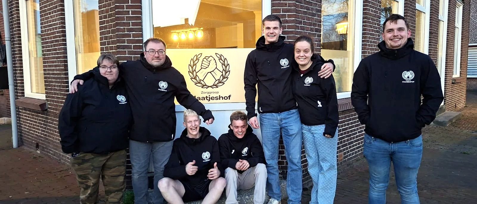 Het team en bewoners van Maatjeshof in truien met het logo, samen voor het pand.