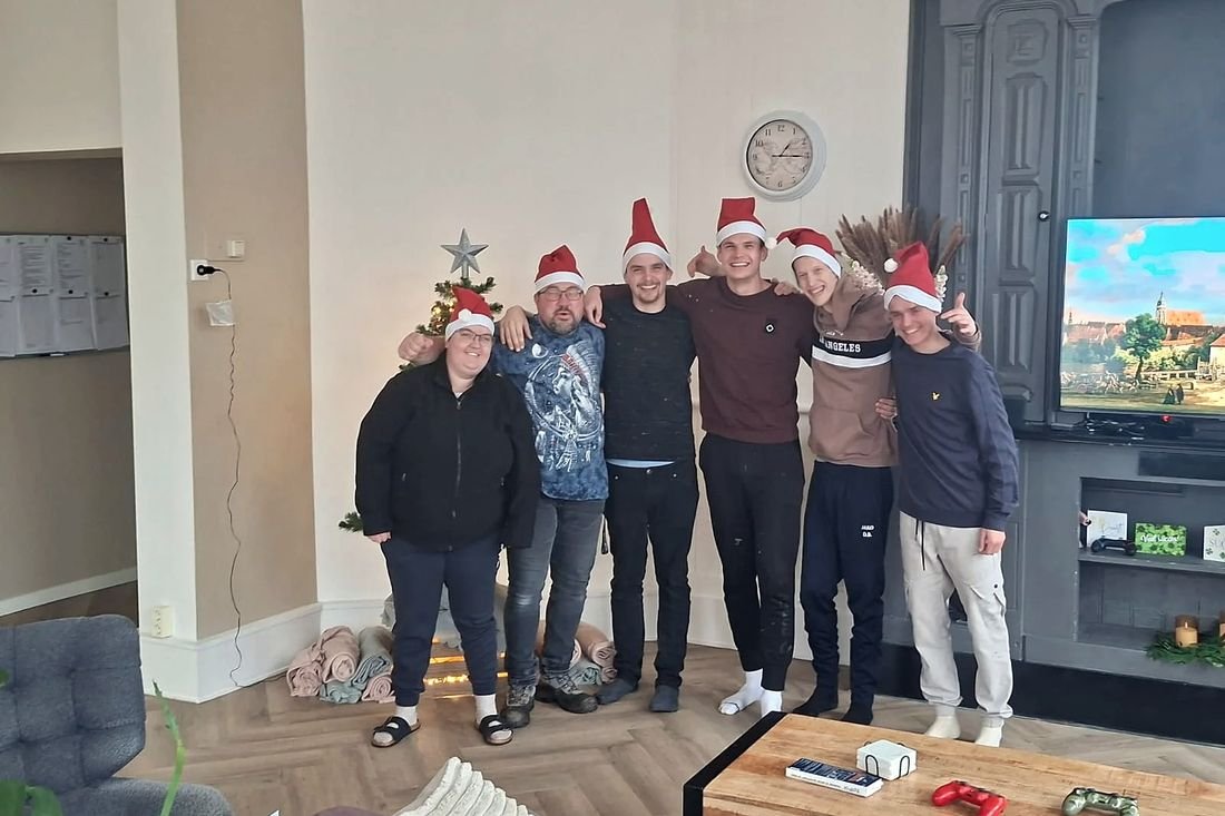 Bewoners en begeleiders met kerstmutsen op staan samen in de woonkamer.