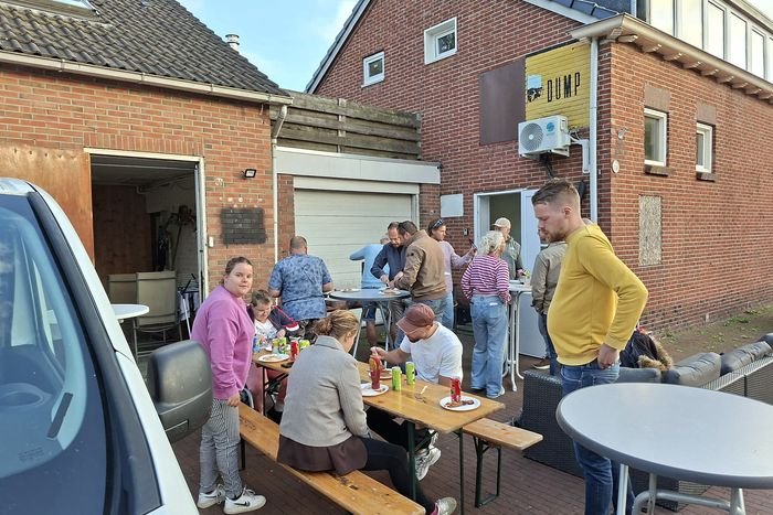 Bewoners en begeleiders eten samen buiten aan picknicktafels in de zon.