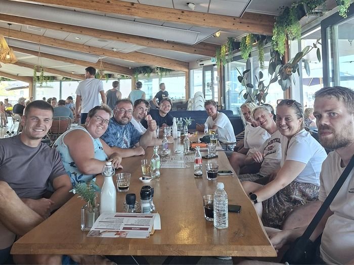 Het team van Maatjeshof zit samen aan een lange tafel in een restaurant en lacht naar de camera.