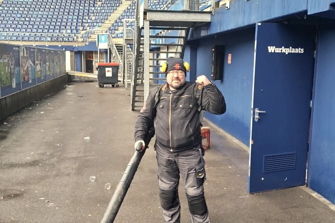 Een bewoner met gehoorbescherming en een bladblazer bij de tribune van het stadion van sc Heerenveen.