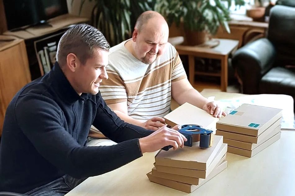 Een begeleider en een bewoner zitten samen aan tafel, met een stapel dozen voor zich.