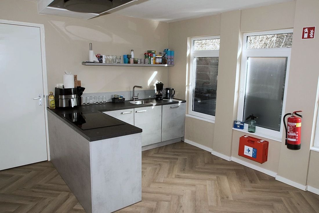 Een gedeelde keuken met een kookeiland, lichte kastjes en een houten visgraatvloer.